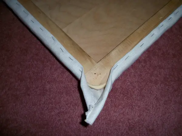 Detalle de cómo tapizar esquinas de un bastidor de madera con tela blanca, asegurada con grapas.